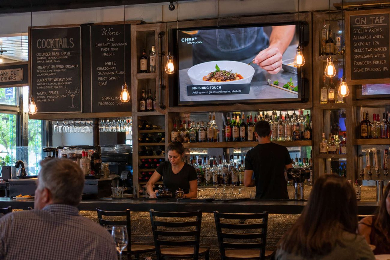 Customers enjoying food and drinks in a restaurant bar with television entertainment.